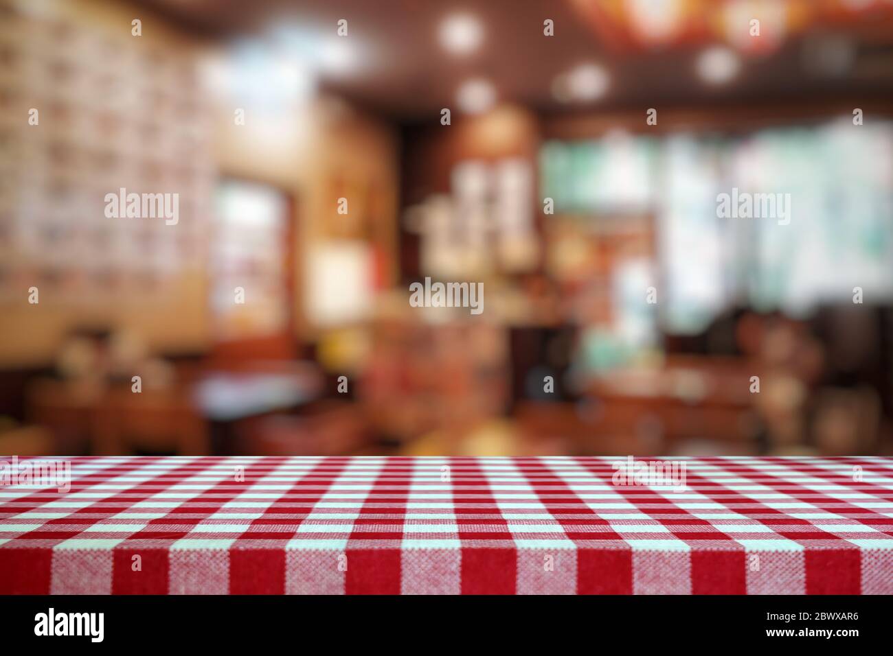 Empty Table Covered with Red Checkered Tablecloth and Blurred Restaurant Background. Stock Photo