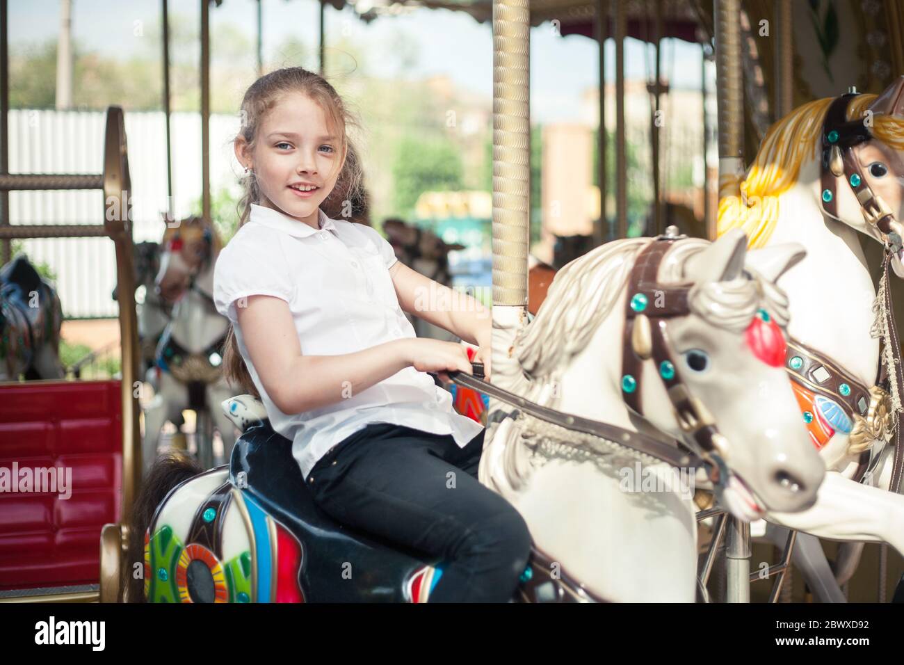 A girl riding a toy horse on a carousel in the park. Stock Photo