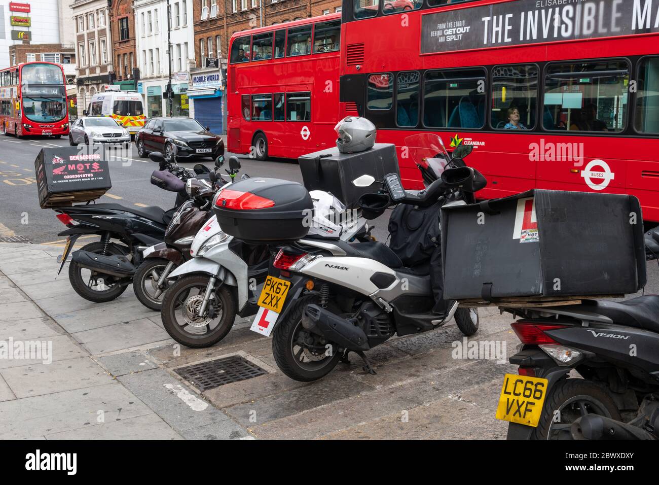 A row of parked motorcycles outfitted for food home delivery with riders near by waiting to pick up orders for delivery. Stock Photo
