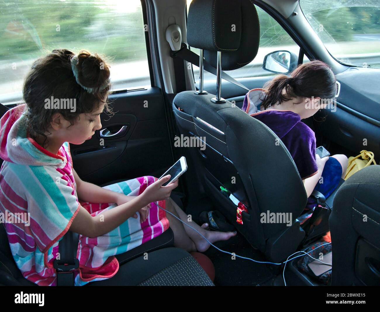 Children travelling in car looking at their smartphones. Stock Photo
