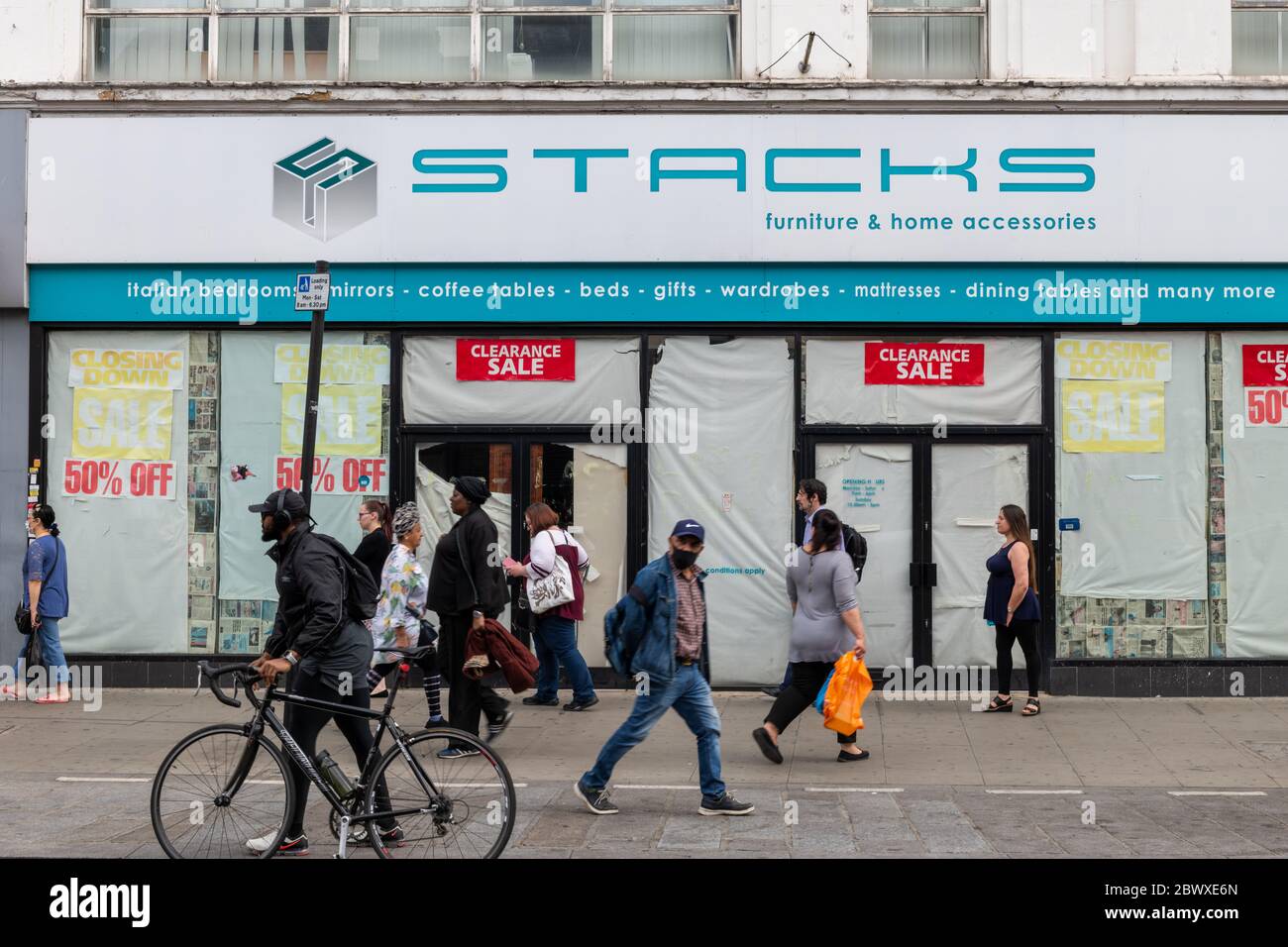 Pedestrians and a cyclist walking pass a closed down high street furniture store. This is a common sight as much of furniture sales have moved online. Stock Photo