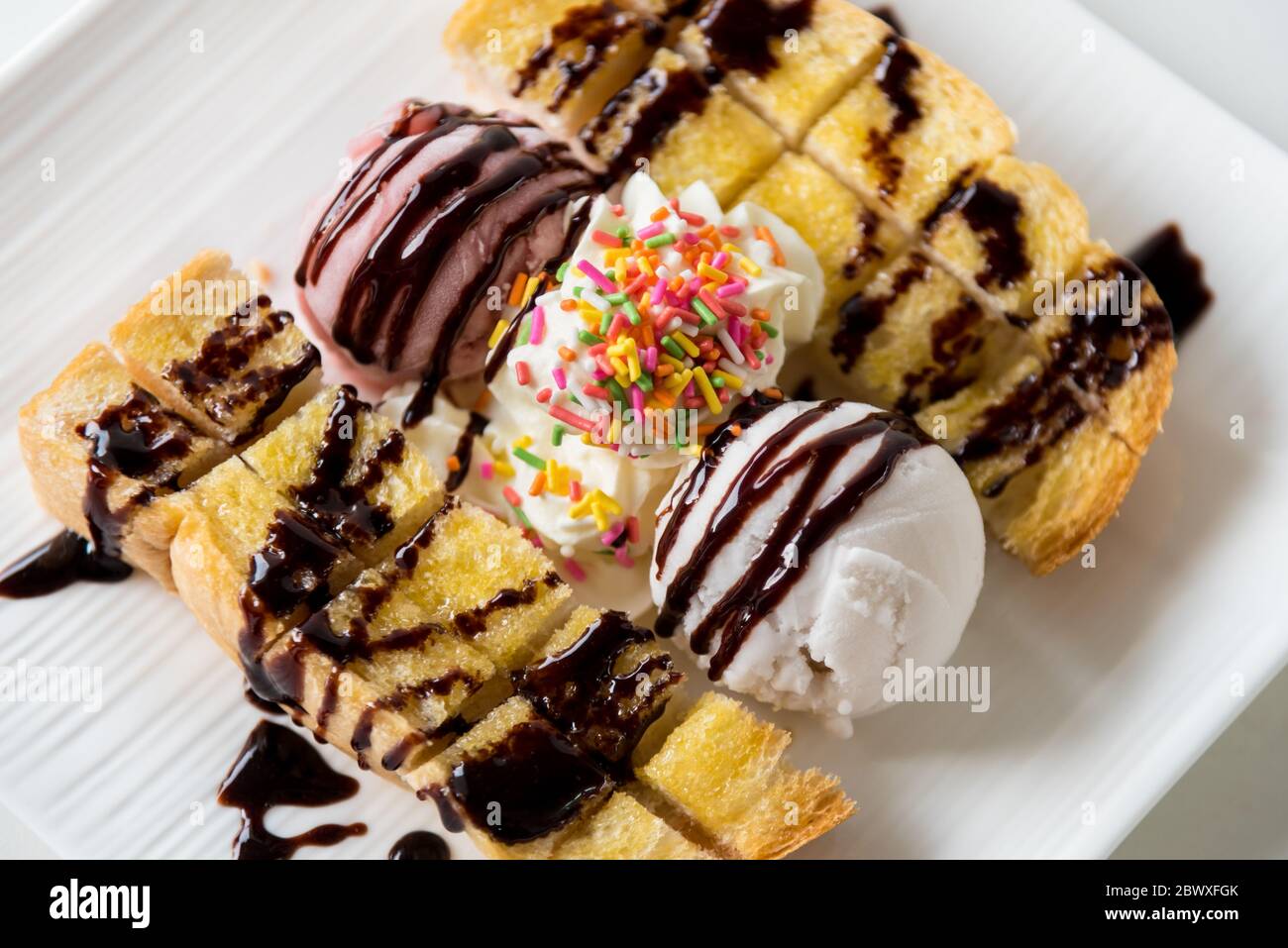 Closeup top view Honey Toast bread served vanilla coconut milk ice cream scoop with chocolate syrup decorate and cream sugar topping sprinkle in a whi Stock Photo