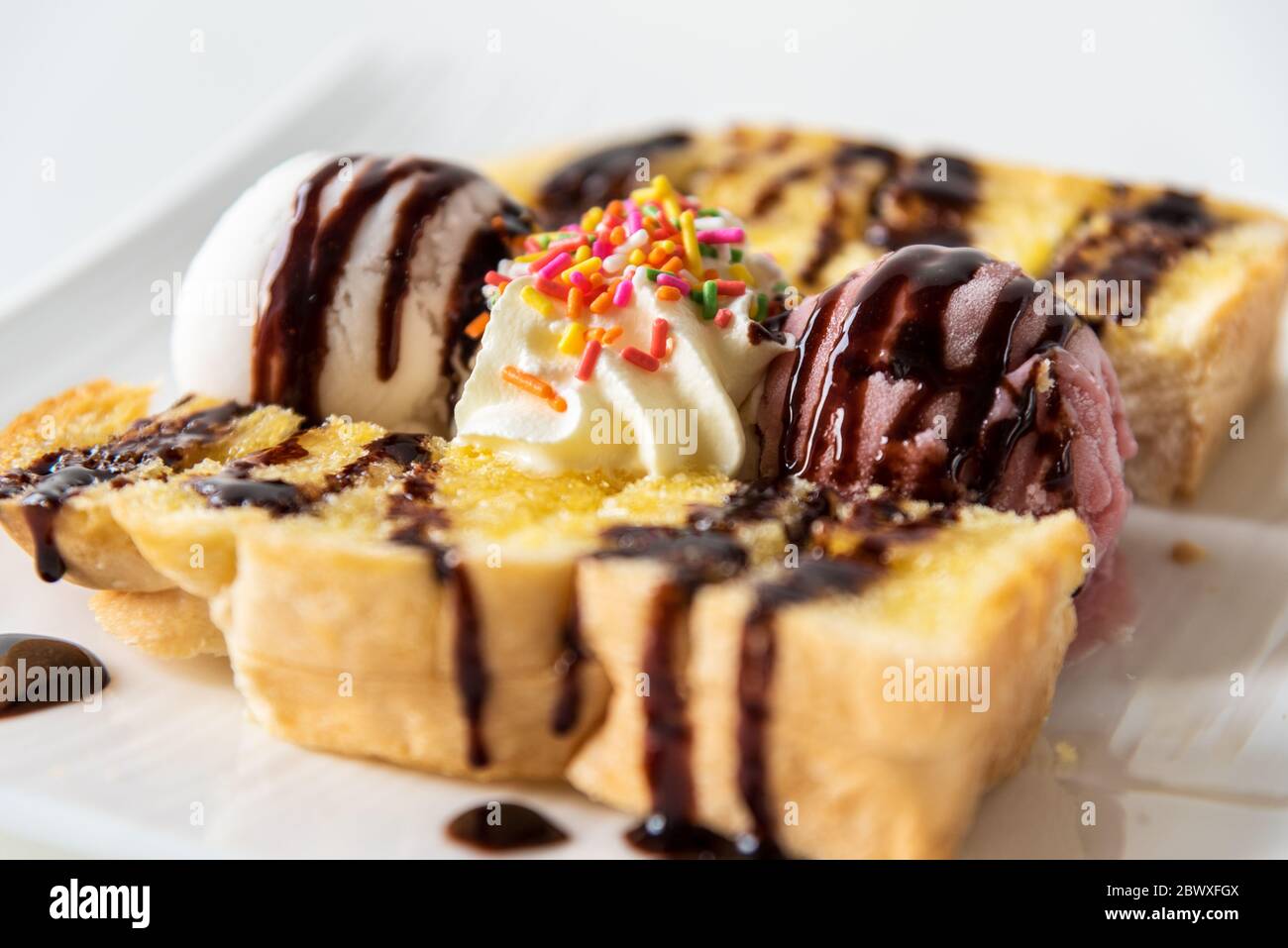 Closeup side view Honey Toast bread and Chocolate brown Ice cream scoop topped with chocolate syrup decorate with a chocolate tablet in a white plate Stock Photo