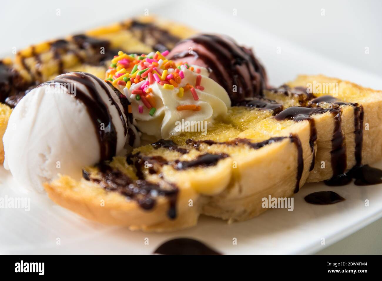 Closeup side view Honey Toast bread and Chocolate brown Ice cream scoop topped with chocolate syrup decorate with a chocolate tablet in a white plate Stock Photo