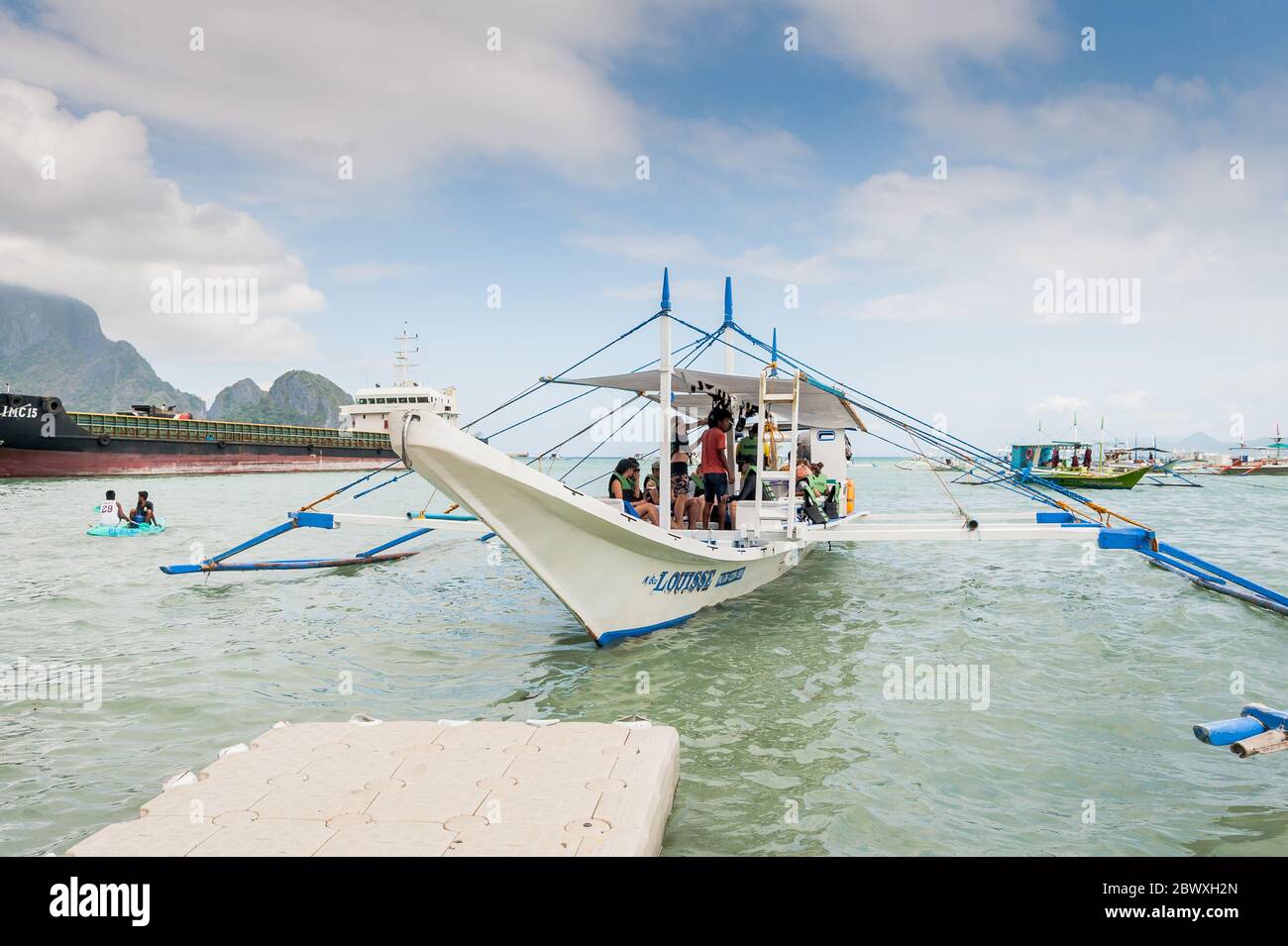 A fisherman's long tail boat loads up with supplies and tourists to head  out on a day trip with a huge oil tanker behind at El Nido Island  Philippines Stock Photo -