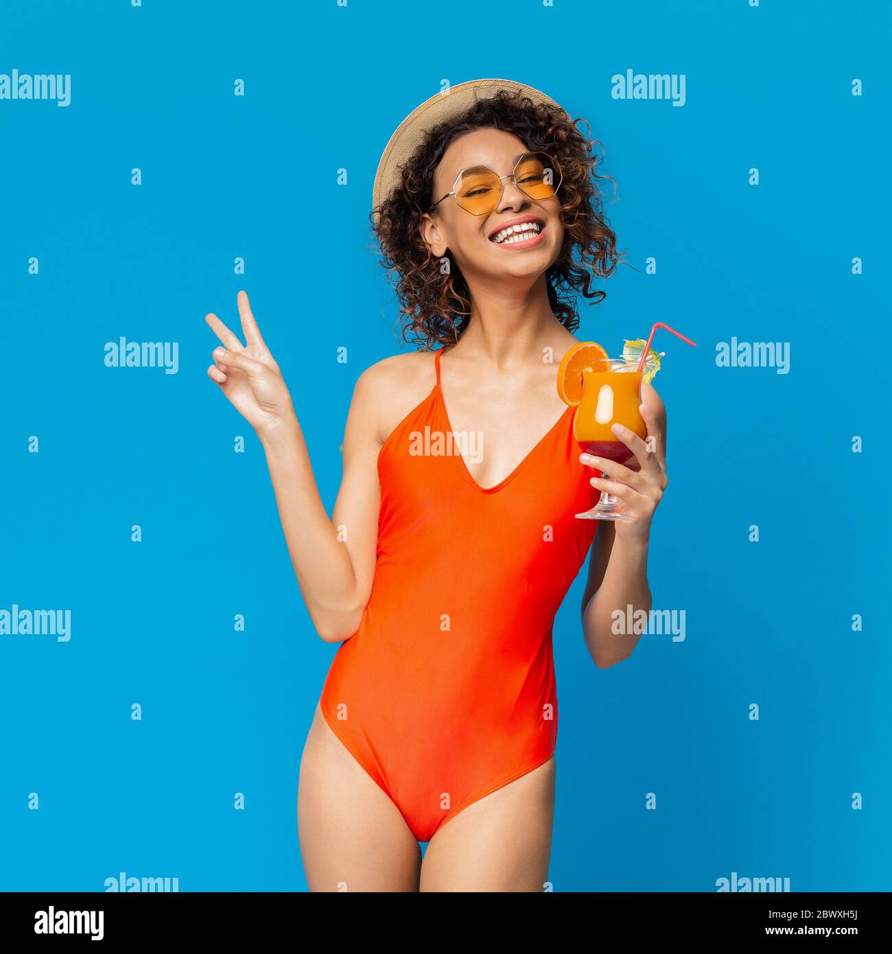 Summer Bliss. Funky Afro Girl In Swimsuit Enjoying Cocktail And Gesturing Peace Stock Photo