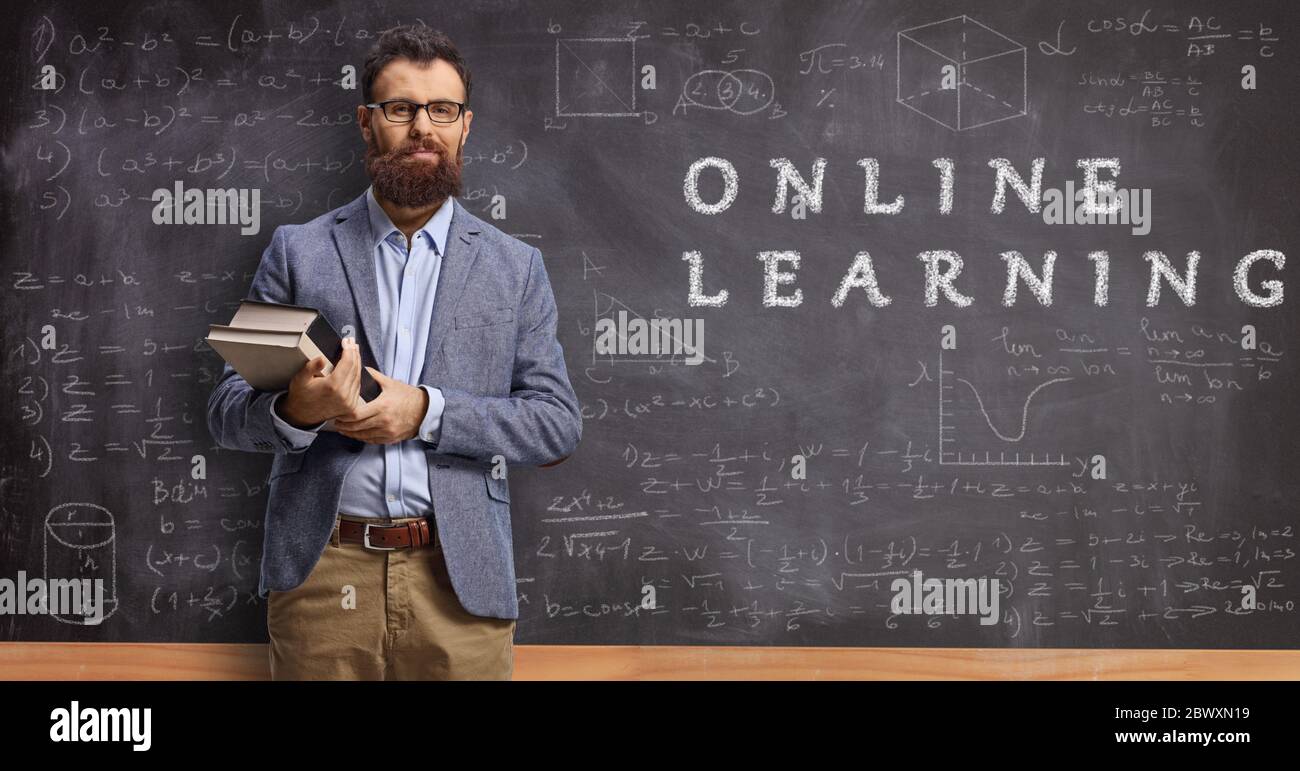 Male teacher holding books and standing in front of a blackboard with text online learning Stock Photo