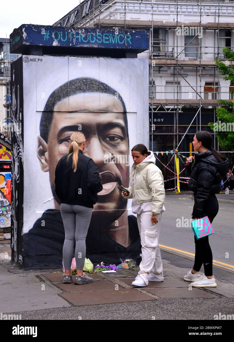 Young women look at a mural depicting George Floyd, painted by street artist Akse, which has recently appeared in Stevenson Square, central Manchester, England, United Kingdom. Floyd, an African-American man, died in Minneapolis, Minnesota, United States, on May 25, 2020, while being arrested by 4 police officers after a shop assistant alleged he tried to pay with a counterfeit $20 bill. Stock Photo