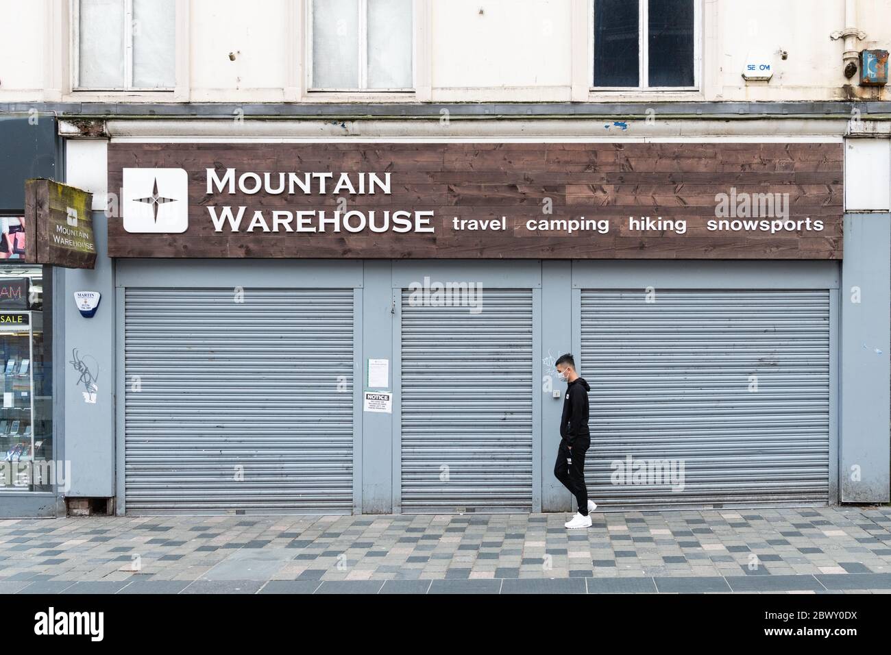 Mountain Warehouse - man wearing face mask walking by a closed and shuttered shop during the coronavirus pandemic lockdown, Glasgow, Scotland, UK Stock Photo