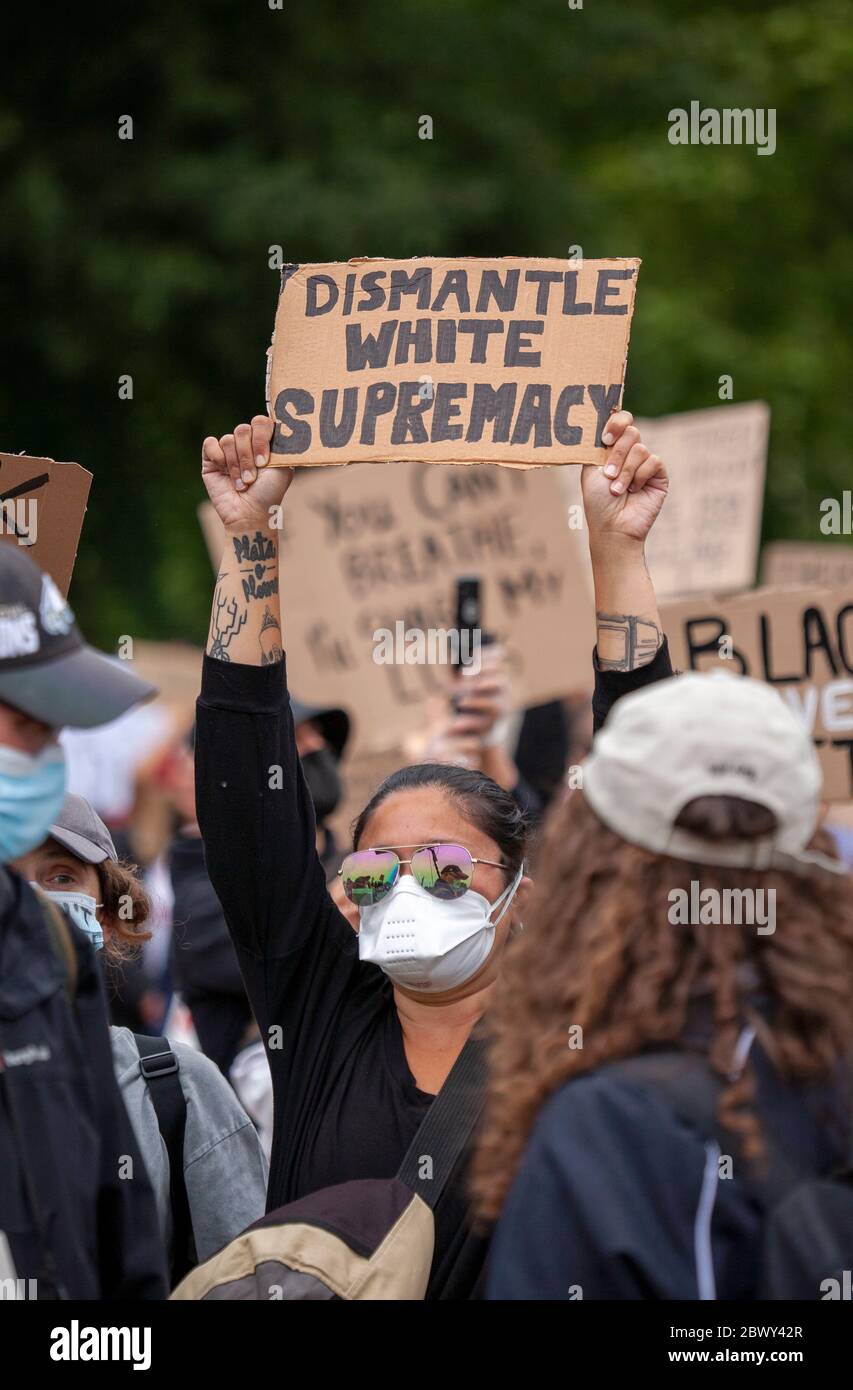 Woman, wearing sunglasses and a face mask, holding up a sign that reads 'Dismantle White Supremacy' during the Black Lives Matter UK protest march. Stock Photo