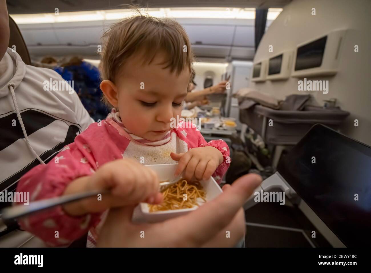 comfortable flight with an infant concept. a little cute hungry toddler sitting in an airplane on his parents lap and eating delicious food on board Stock Photo