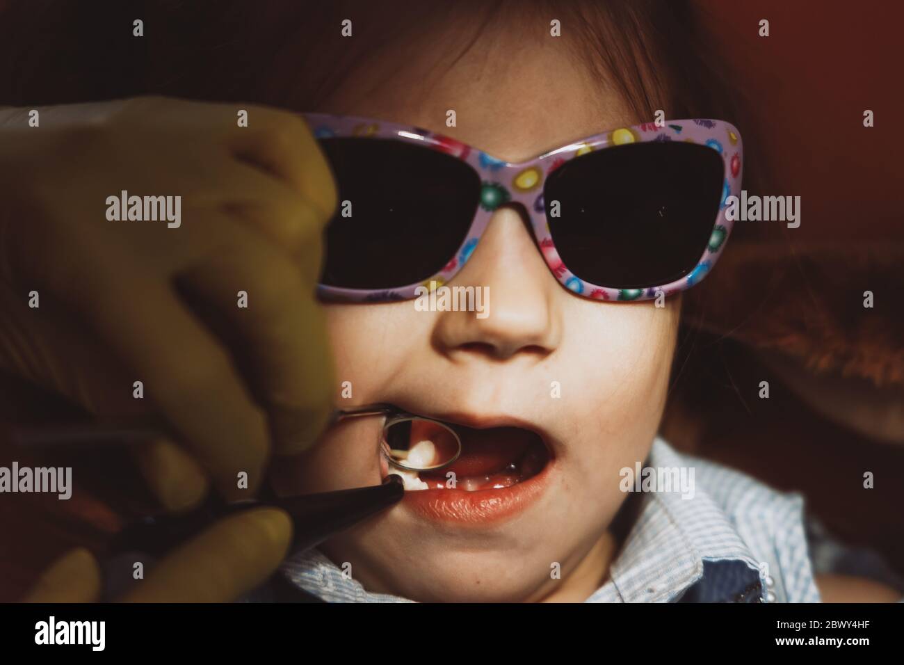 Closeup crop dentist in gloves using mirror to examine teeth of little