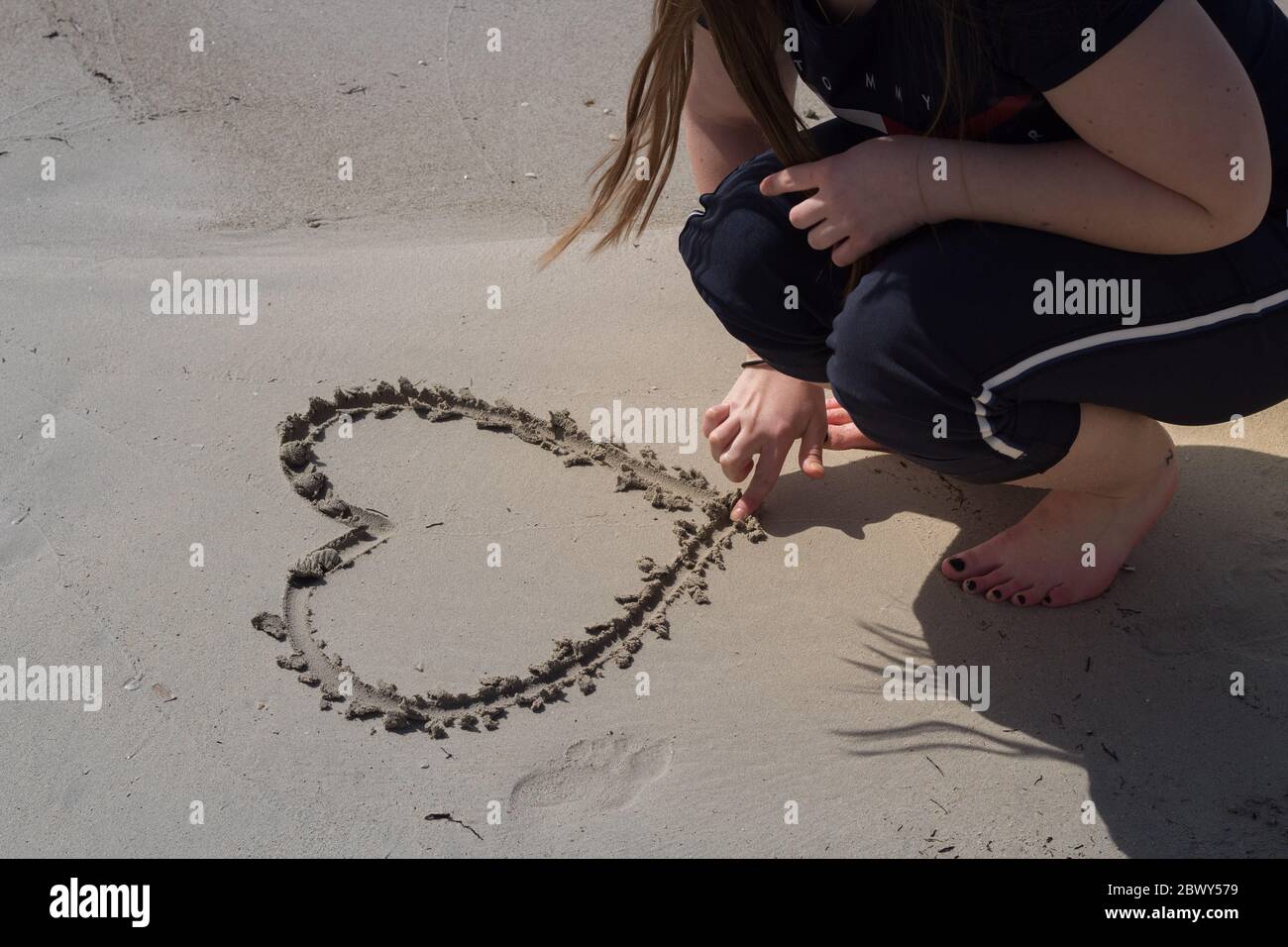 Girl/ Woman drawing a heart in the sand at the beach Stock Photo