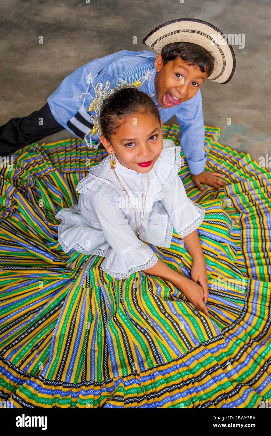 A school girl in traditional dress sitting on the floor in the community of San Carlos near Panama City, Panama with a boy goofing off. Stock Photo