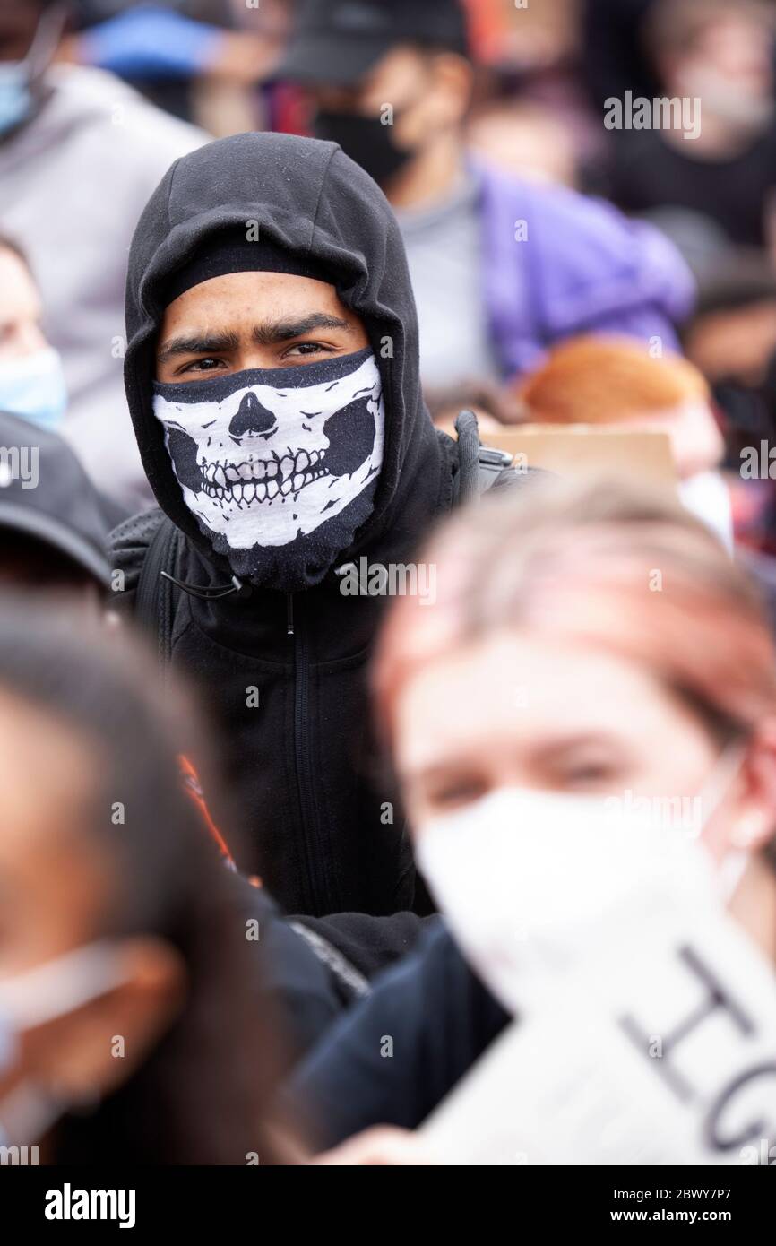 Man, wearing a hoody and skeleton face mask sits in a crowded Hyde park during the Black Lives Matter UK protest march. London, England, UK Stock Photo