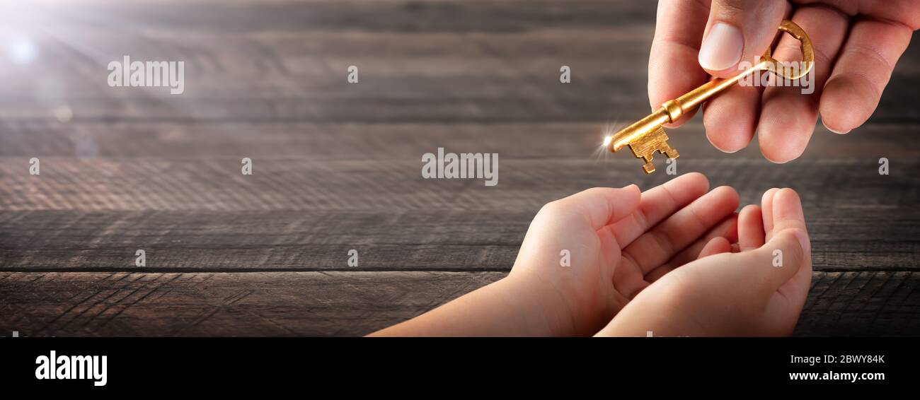 Hand Of Father Giving Old Golden Key To Child - Inheritance Concept Stock Photo