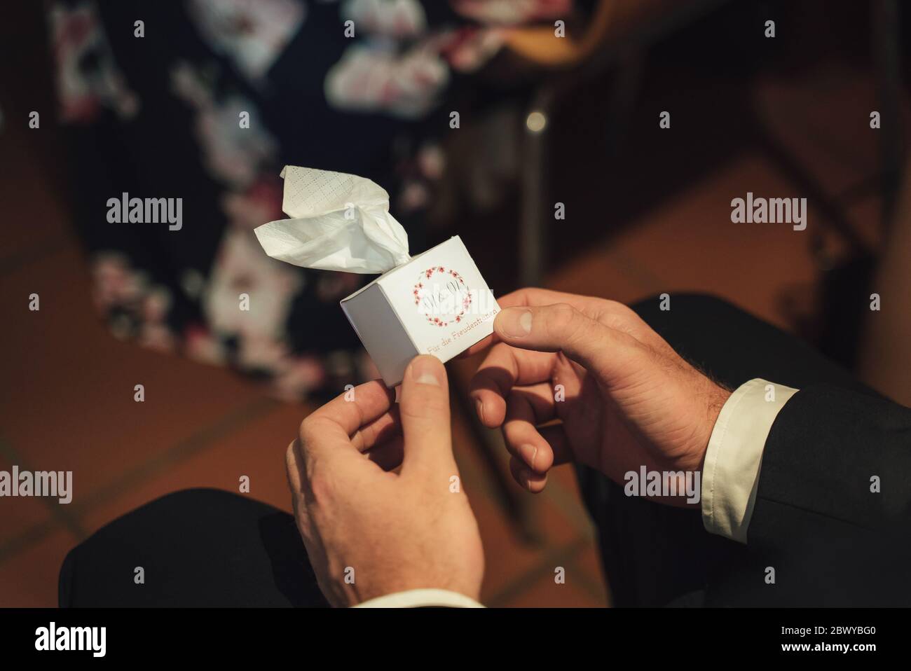 Closeup photo of formal clothed male hands holding small shite box of paper tissues. Translation: 'For tears of happiness'. Wedding day concept. Stock Photo