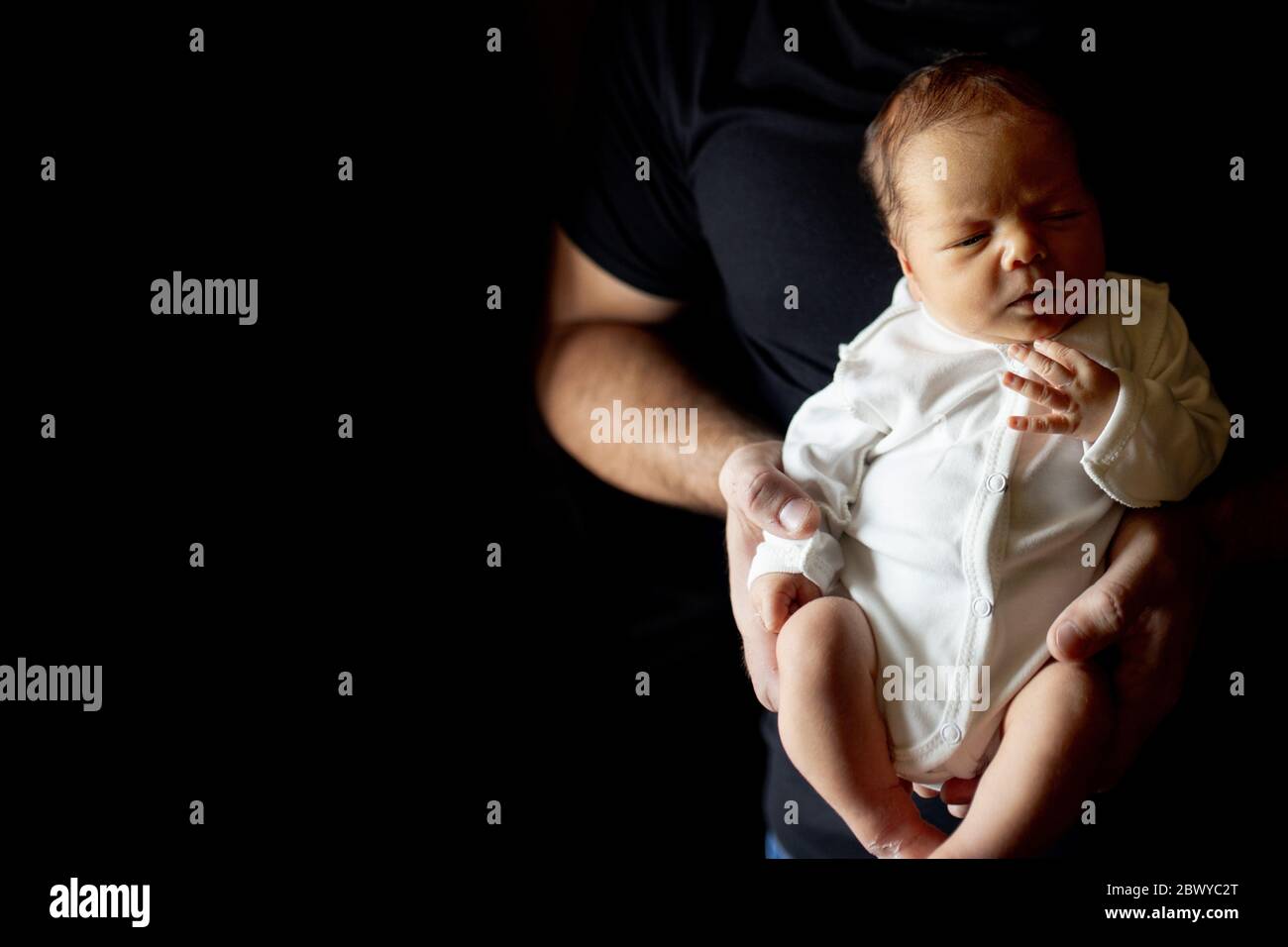 Father holding his 15 days old son in his hand on black background Stock Photo
