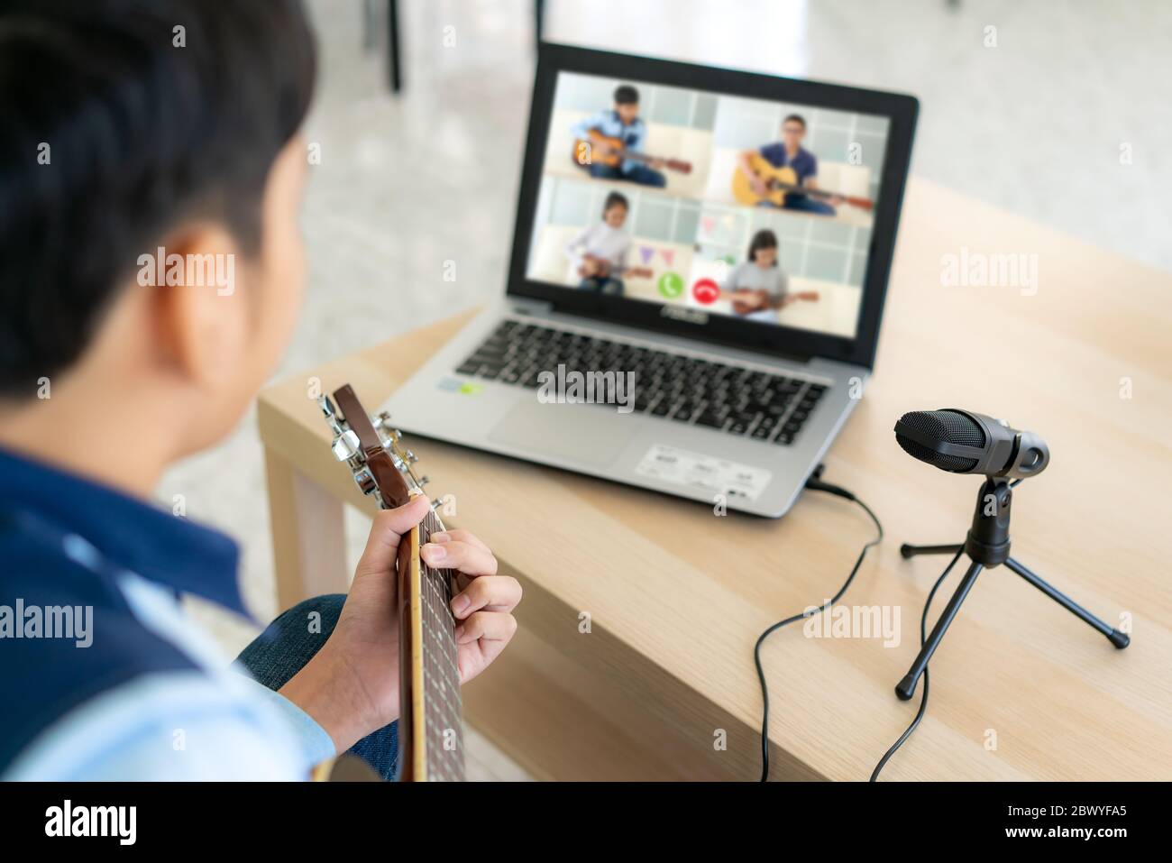 Asian boy playing acoustic guitar virtual happy hour meeting for play music online together with friend in video conference with laptop for a online m Stock Photo