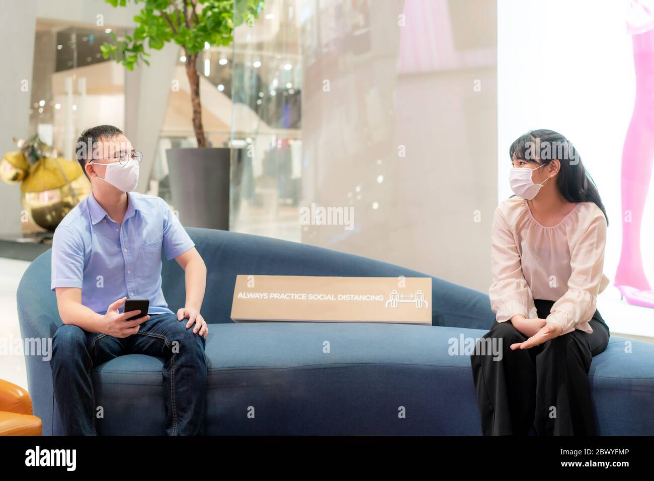 Two Asian young man and woman wearing mask and talking with friend while sitting distance of 6 feet distance protect from COVID-19 viruses for social Stock Photo
