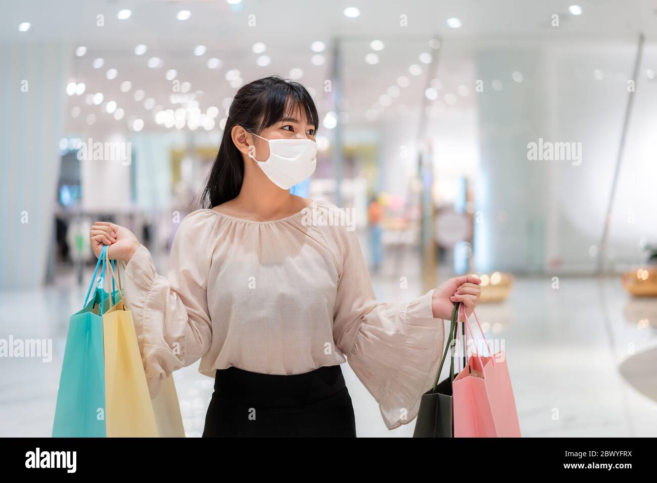 Asian woman wearing mask over her face while walking at shopping mall