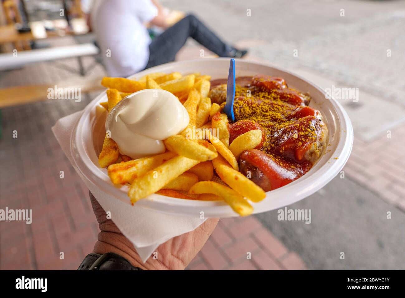 Hand hold Currywurst, grilled pork sausage on top with curry powder served with curry ketchup