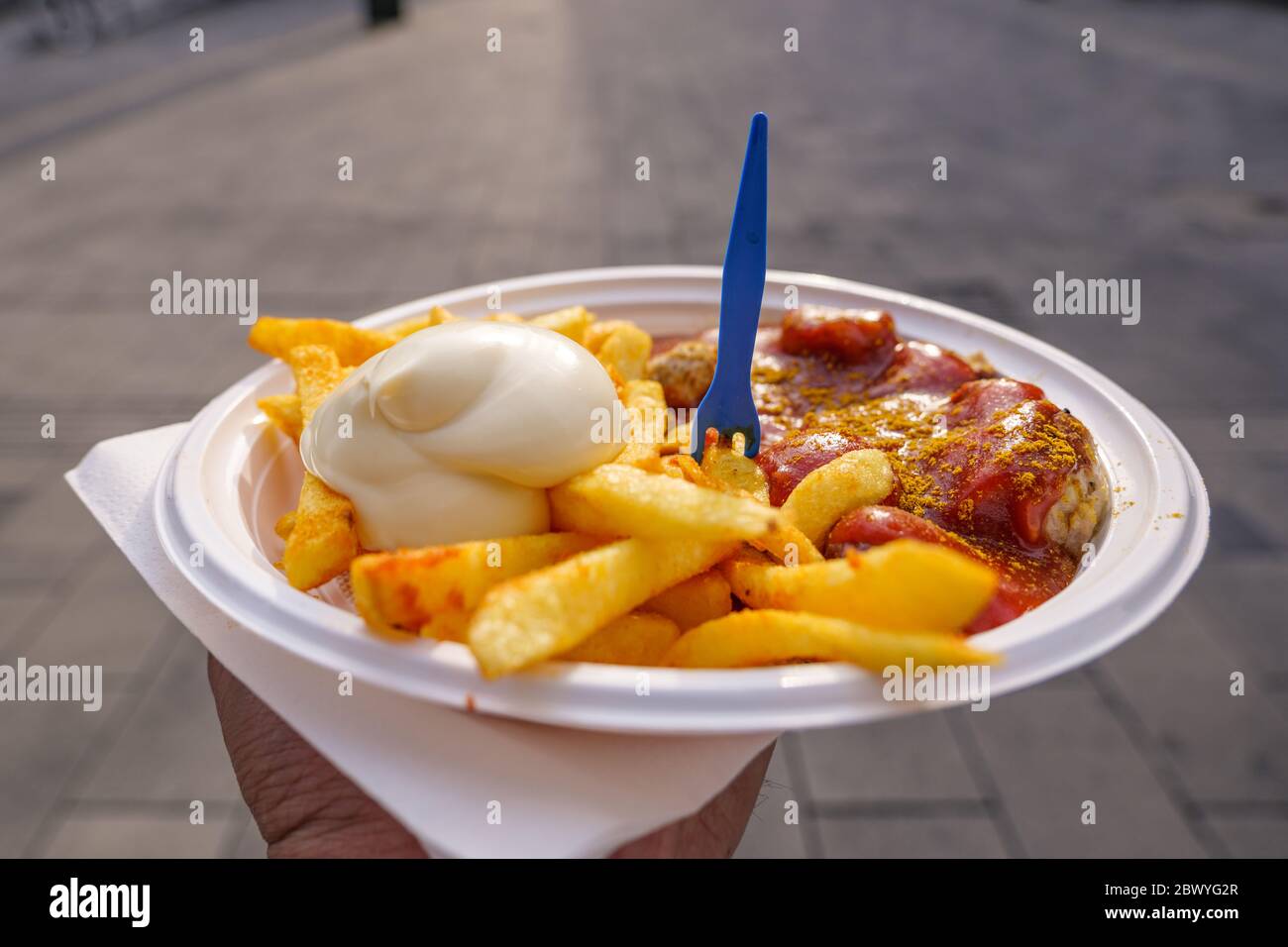 Hand hold Currywurst, grilled pork sausage on top with curry powder served with curry ketchup