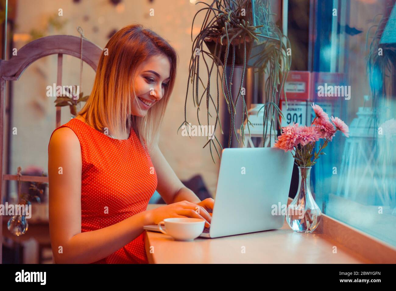 Charming woman with beautiful smile looking working on laptop during rest in coffee shop or in home happy. Caucasian female watching her photos on pc Stock Photo