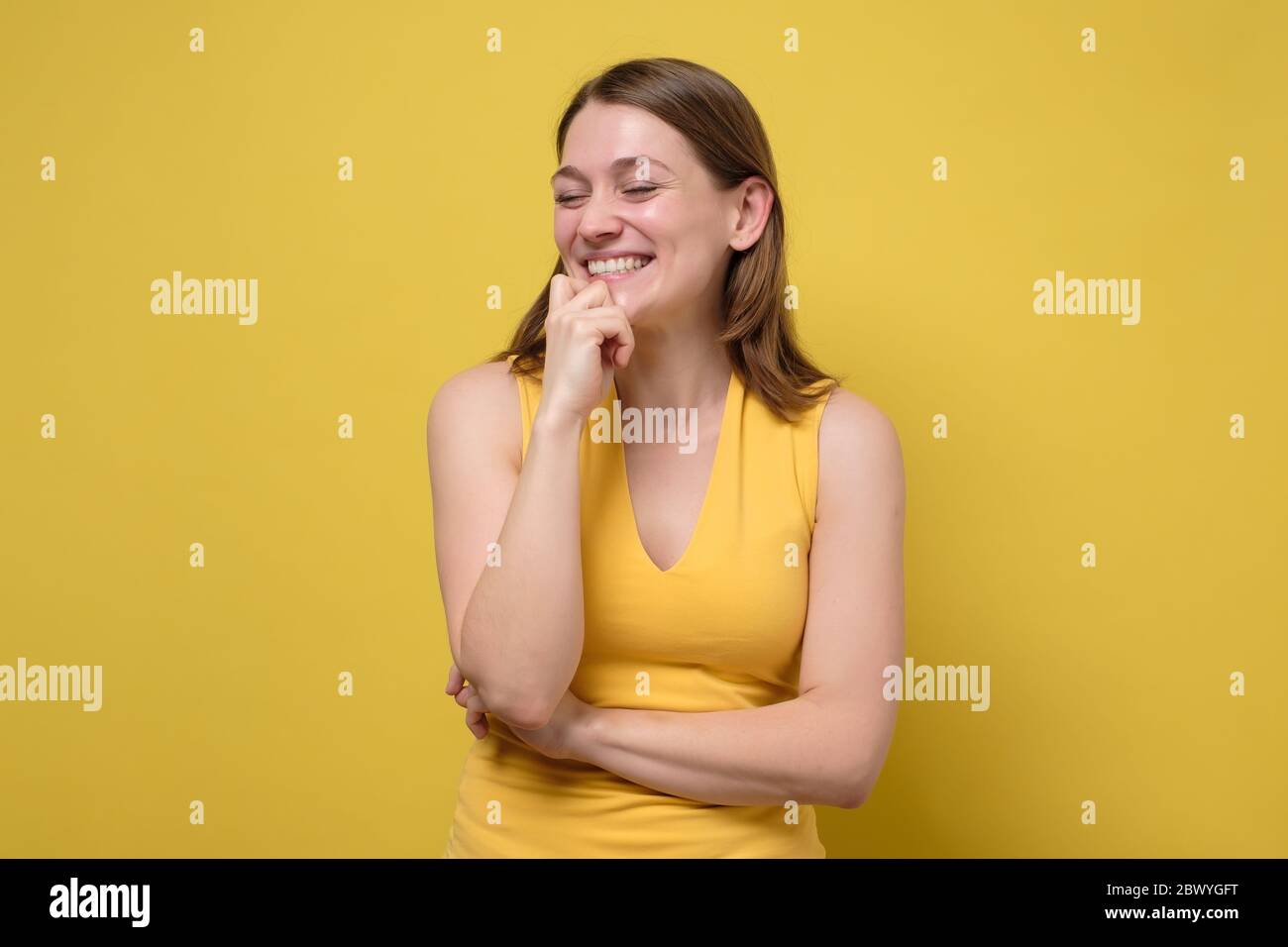 Joyful friendly looking woman laugh out loud not hiding emotions giggling hear funny hilarious joke from friend. Studio shot on yellow wall. Stock Photo