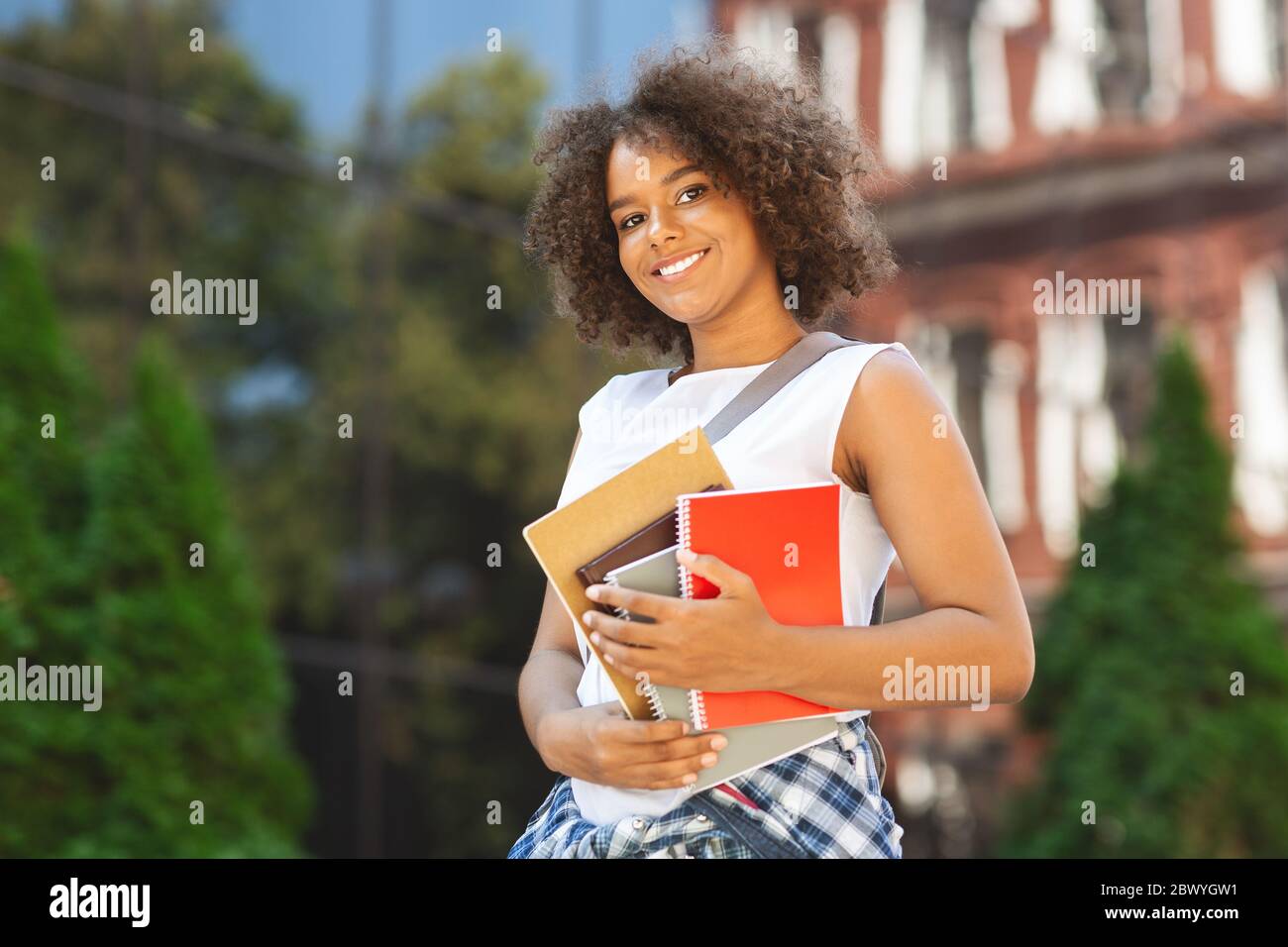Student Orientation Concept. Happy black teen girl holding workbooks posing outdoors Stock Photo