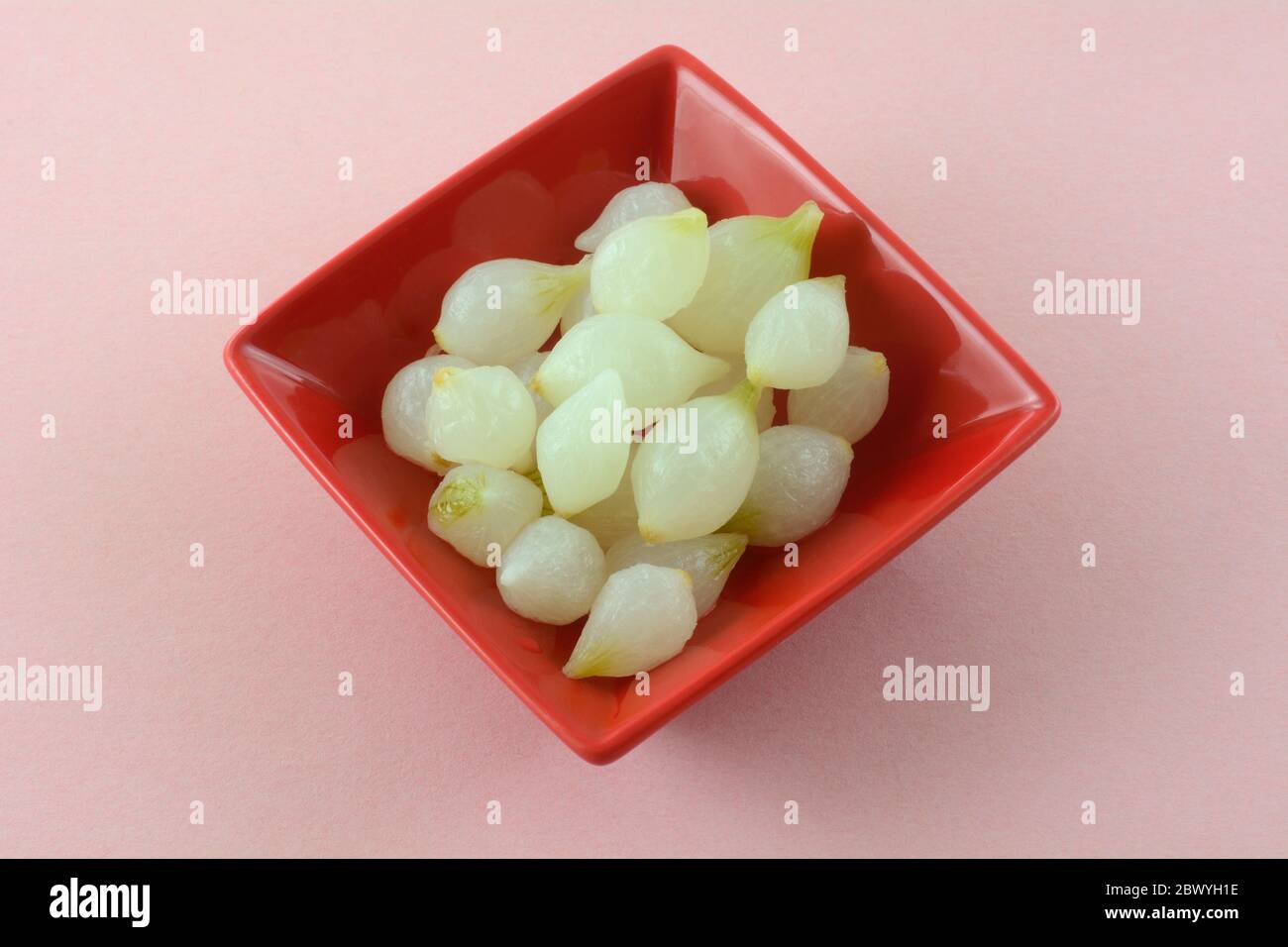 Fresh pearl onions in red condiment bowl on pink background Stock Photo