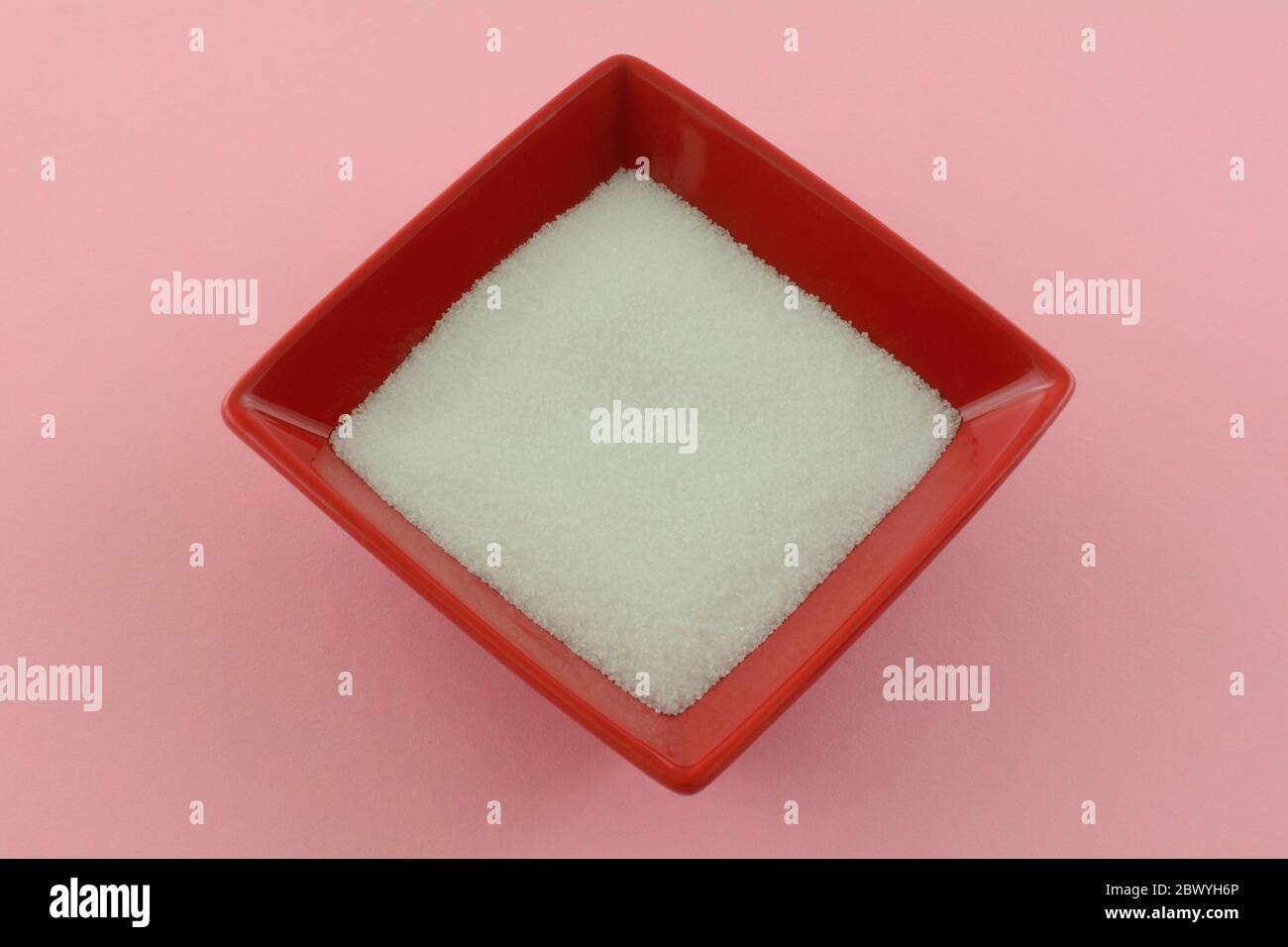 White granulated sugar in square red sugar bowl on pink background Stock Photo