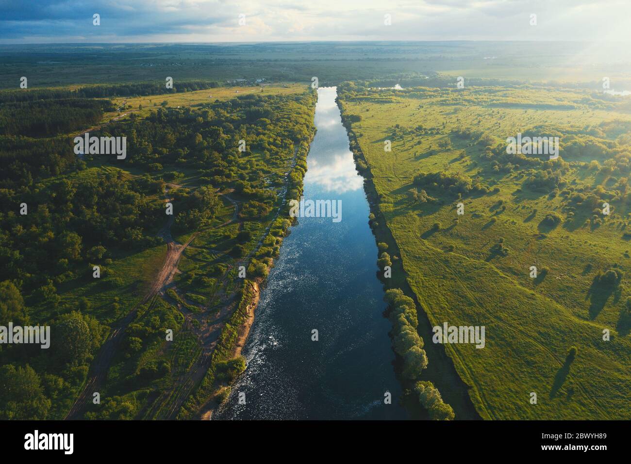 Beautiful summer sunset over blue river among green meadows, freedom nature landscape, aerial panorama from drone. Stock Photo
