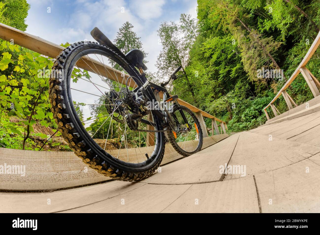 Photo of a mountain bike standing on a forest river stream wooden bridge road, rear wheel angle view Stock Photo