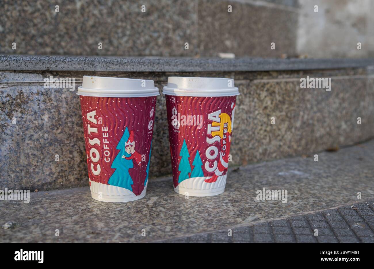 Two used disposable Costa Coffee cups with a Christmas themed design left on a set of outside stairs. London Stock Photo