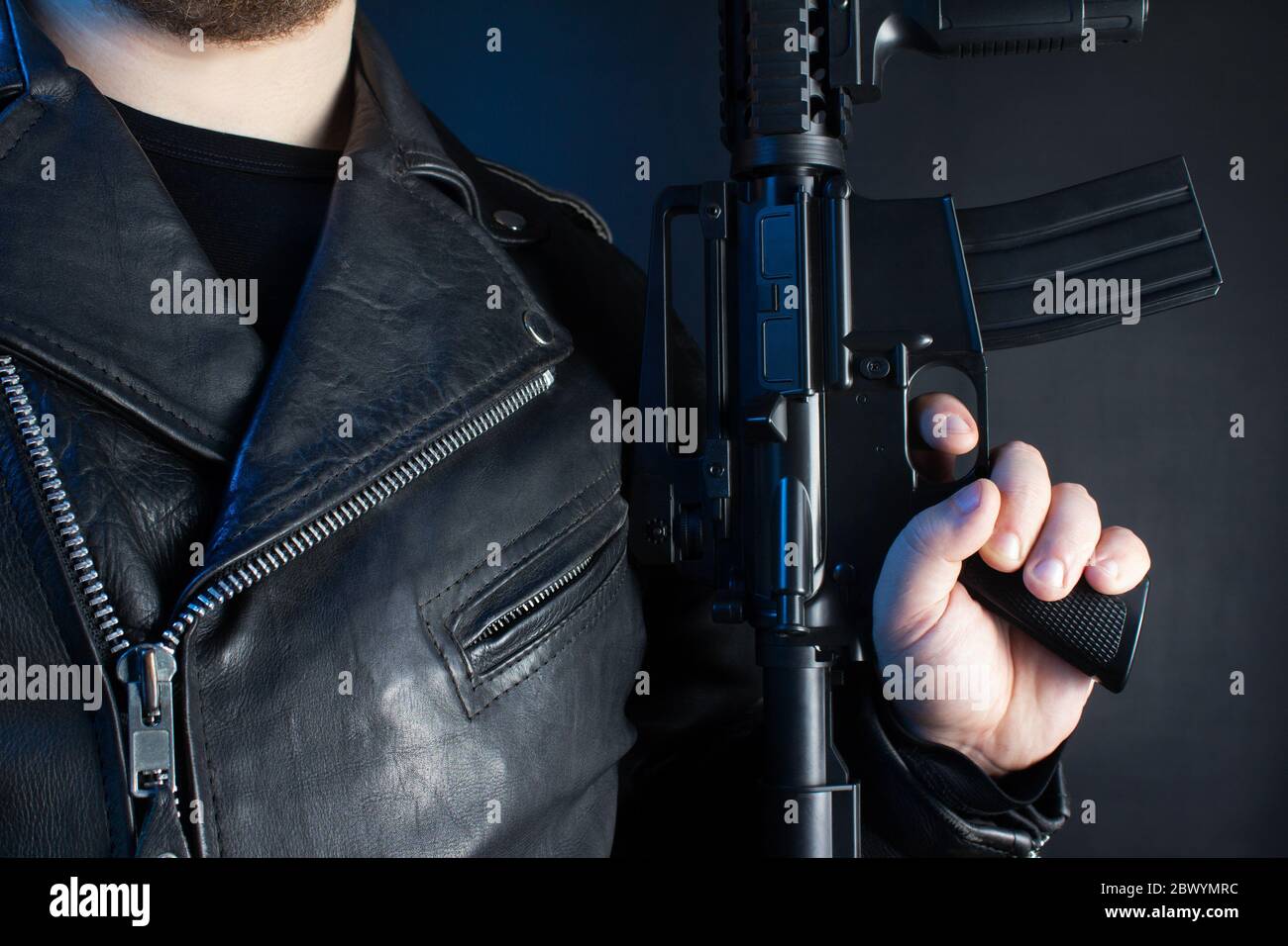 Photo of a biker in black leather jacket with skull rings holding rifle on black background. Stock Photo