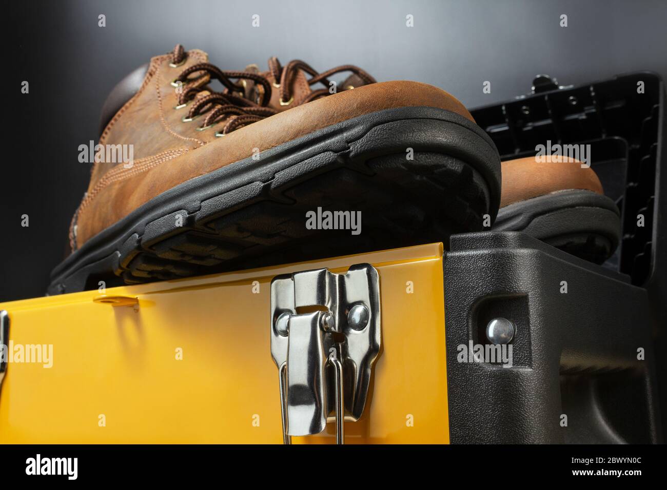 Worker leather boots standing on yellow toolbox on black background. Stock Photo