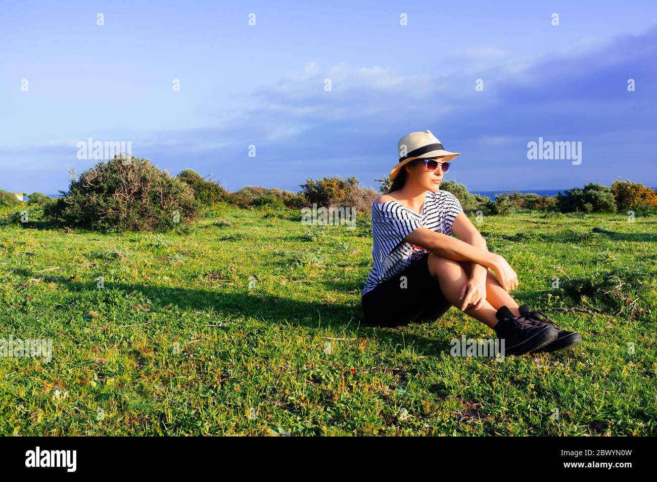 Beautiful young woman enjoying nature sitting on green grass sunning Stock Photo