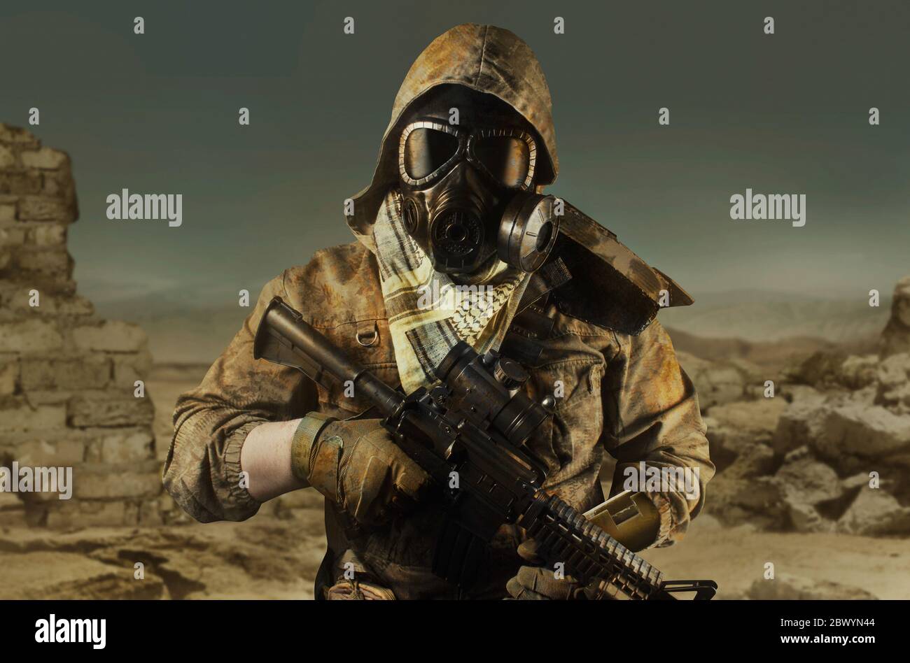Photo of a desert post-apocalyptic soldier in tactical jacket, gas mask, gloves, rifle and armor on wasteland background front view. Stock Photo