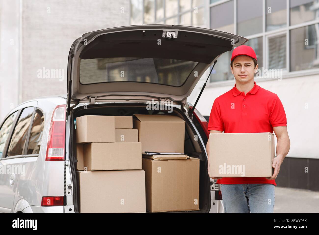 Home delivery from online store. Courier delivers parcel to door, stands near car Stock Photo