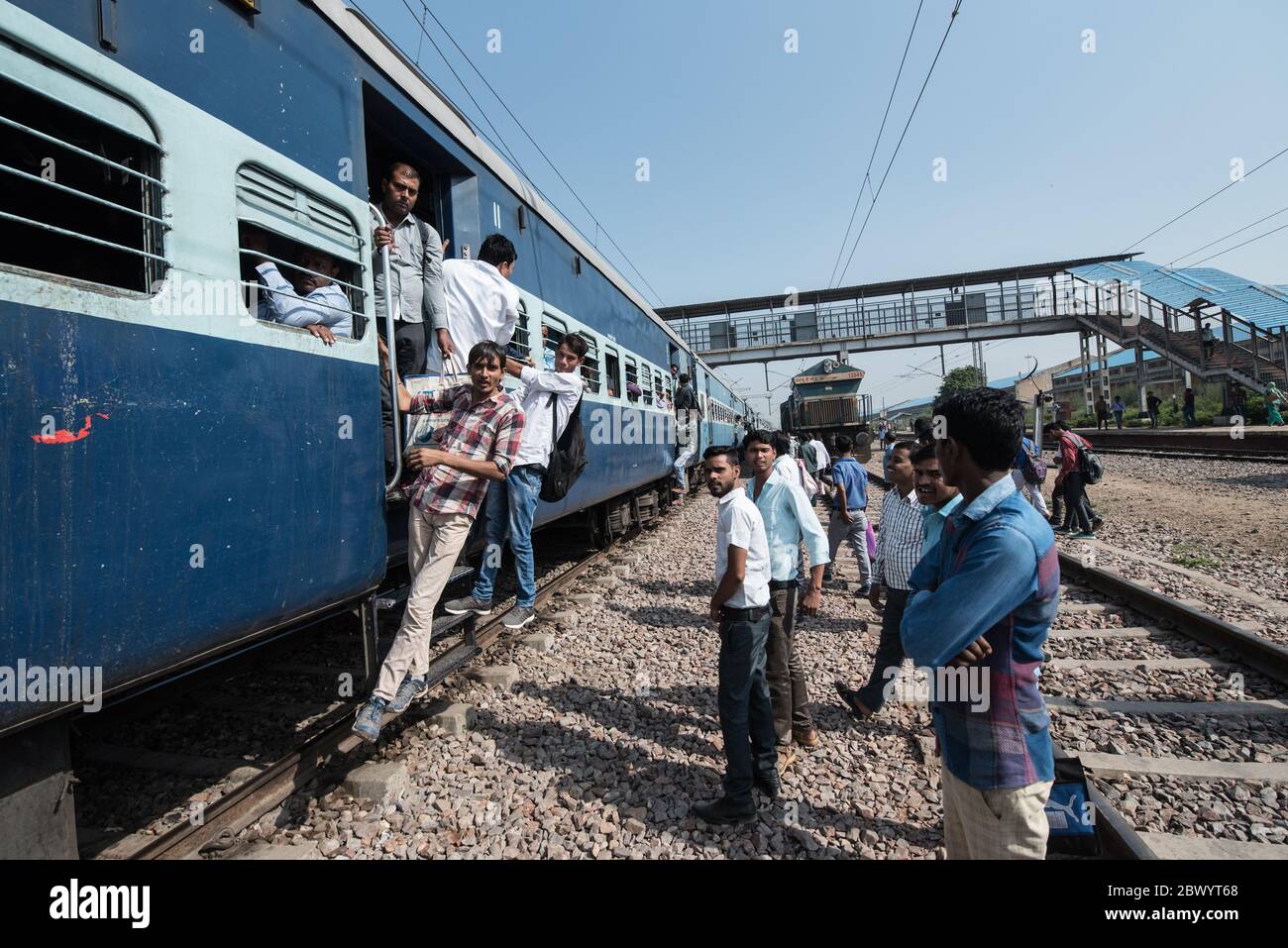 Commuters hang out of an overcrowded Indian Railways train, at Noli Railway Station near
