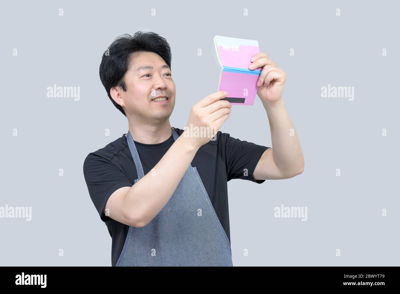 A middle-aged Asian man holding a bank passbook in his hand on a gray background. Stock Photo