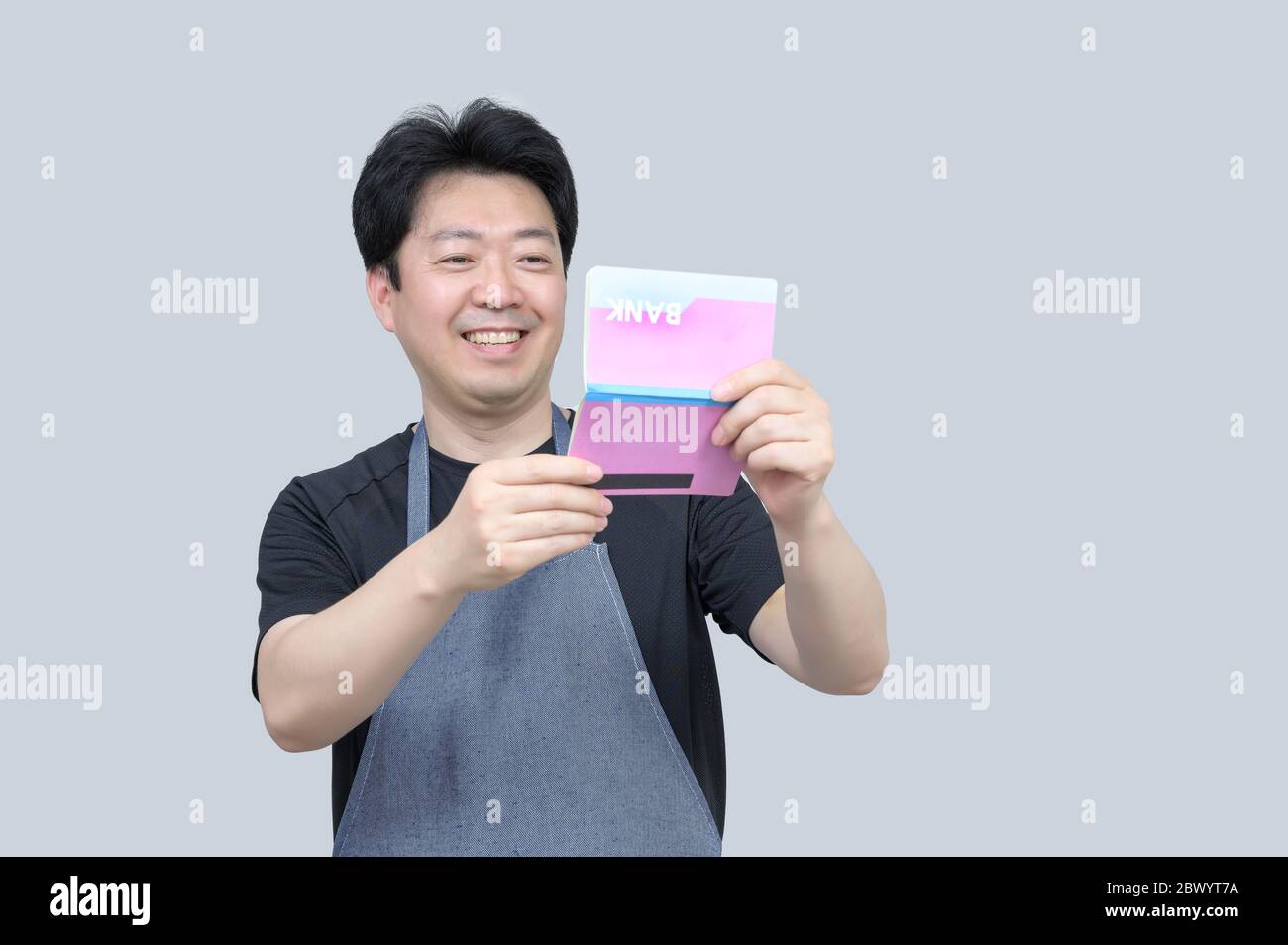 A middle-aged Asian man holding a bank passbook in his hand on a gray background. Stock Photo