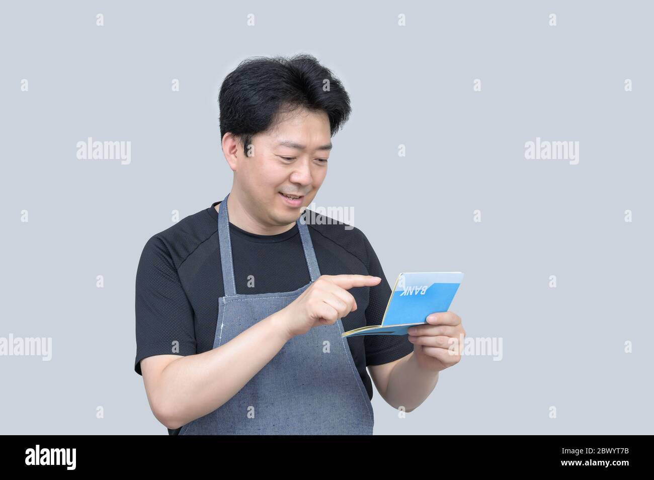 A middle-aged Asian man holding a bank passbook in his hand on a gray background. Stock Photo