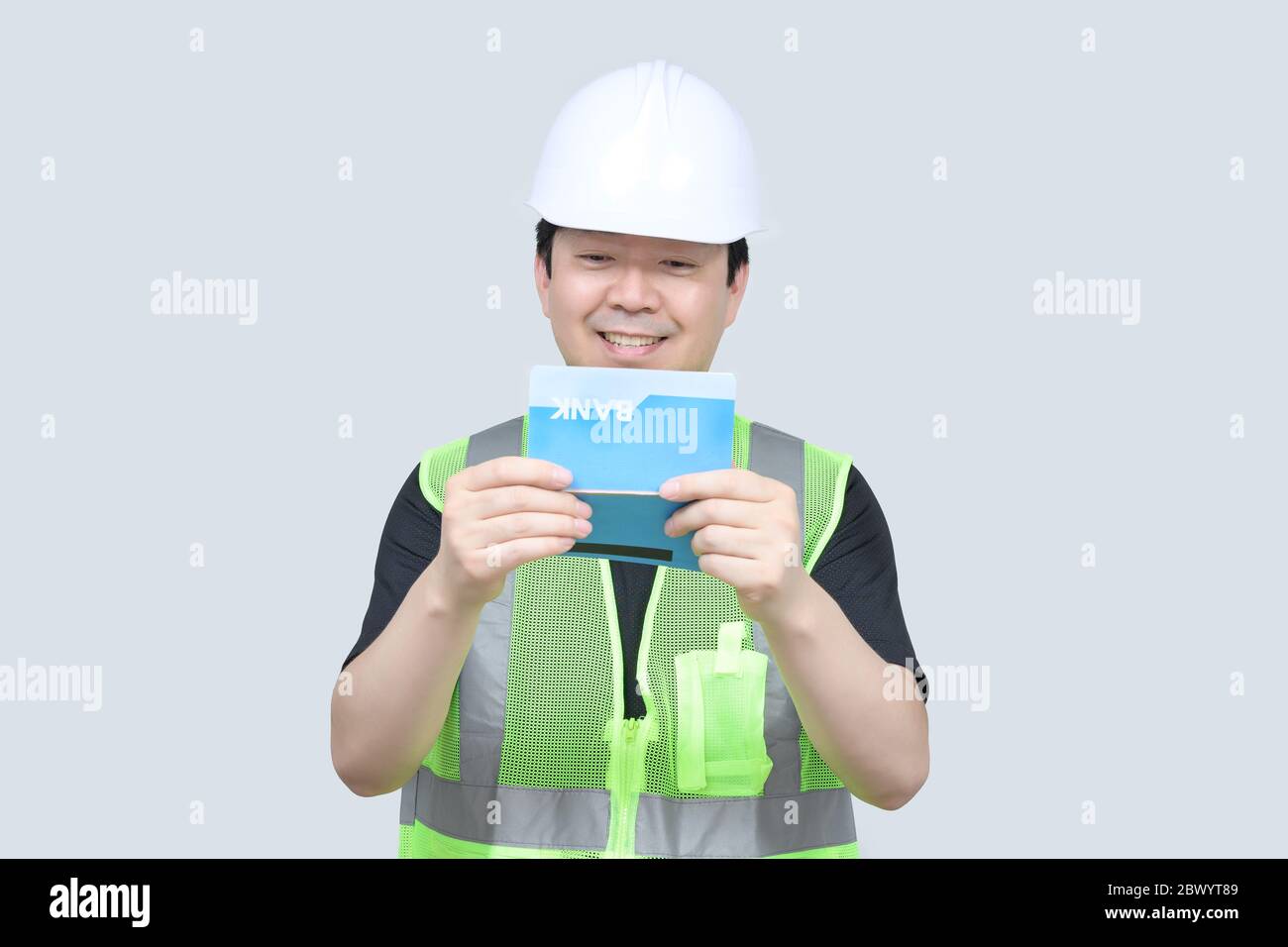 A middle-aged Asian engineer holding a bank passbook in his hand on a gray background. Stock Photo