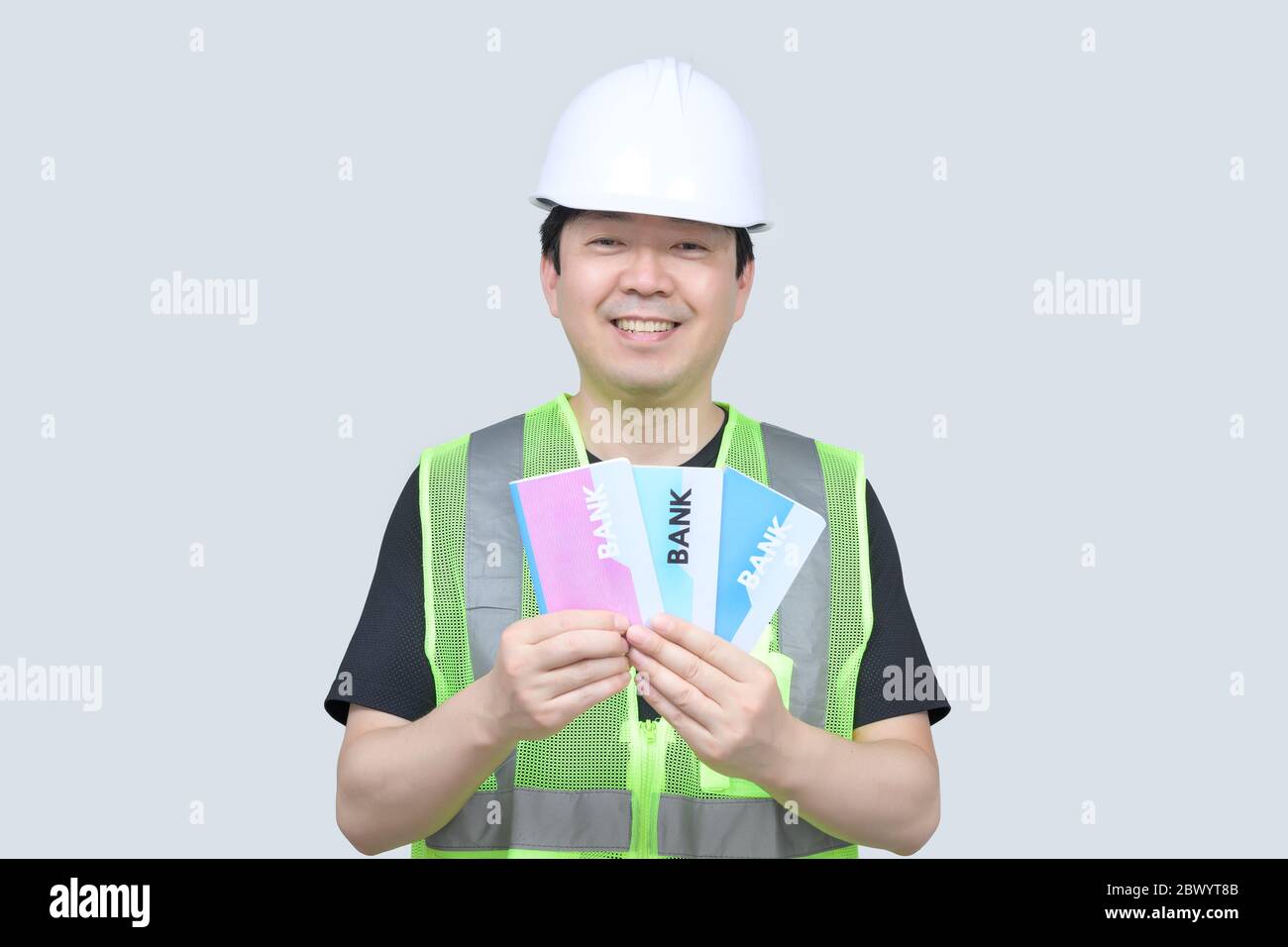 A middle-aged Asian engineer holding a bank passbook in his hand on a gray background. Stock Photo
