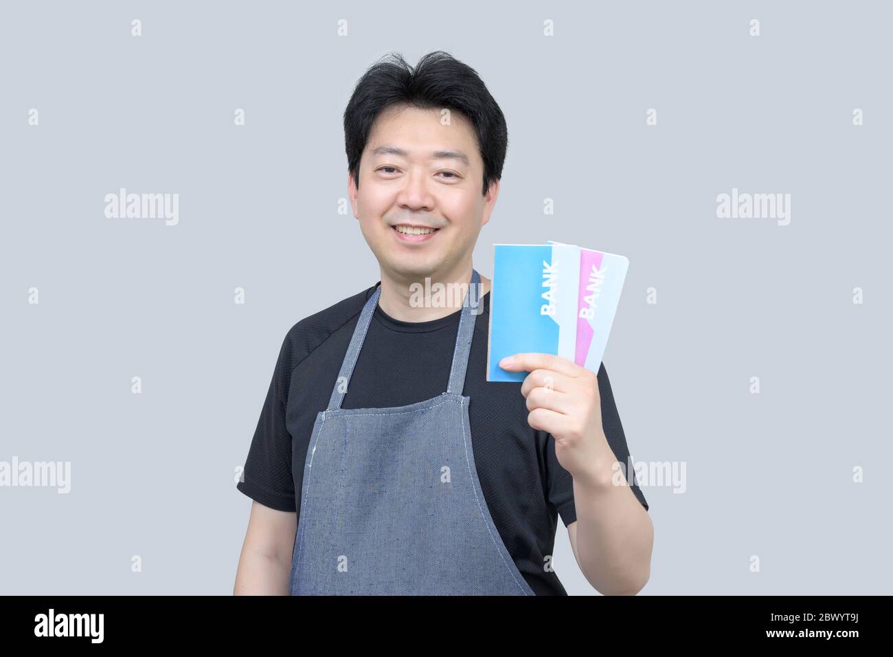 A middle-aged Asian man holding a bank passbook in his hand on a gray background. Stock Photo