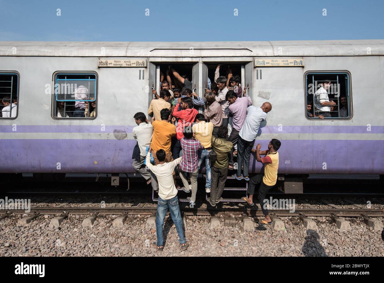 Commuters hang out of an overcrowded Indian Railways train, at Noli Railway Station near