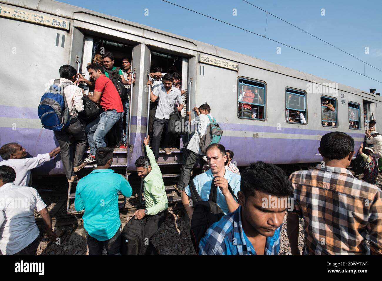 Commuters hang out of an overcrowded Indian Railways train, at Noli Railway Station near Ghaziabad, New Delhi, India. Stock Photo