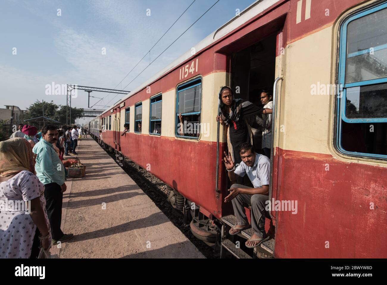 Commuters hang out of an overcrowded Indian Railways train, at Noli Railway Station near